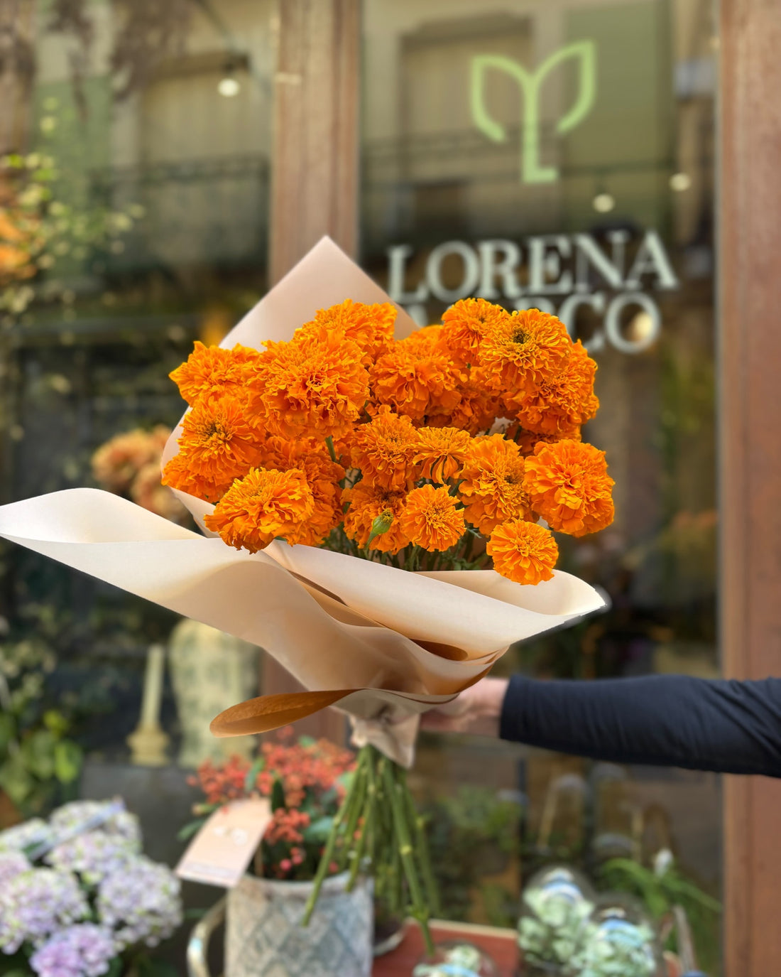 Paquete de cempasúchil naranja envuelto en papel, delante del escaparate de Lorena Marco en C/ Ruda 15, Madrid