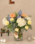 Ramo de hortensias pastel con flores en tonos crema, melocotón y azul suave, en jarrón de cristal