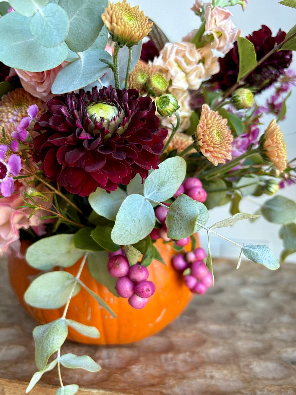 Detalle de flores burdeos, rosas y eucalipto sobre una calabaza naranja